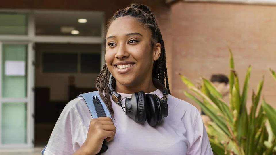 Étudiante souriante avec son sac à dos et ses cahiers sur le campus