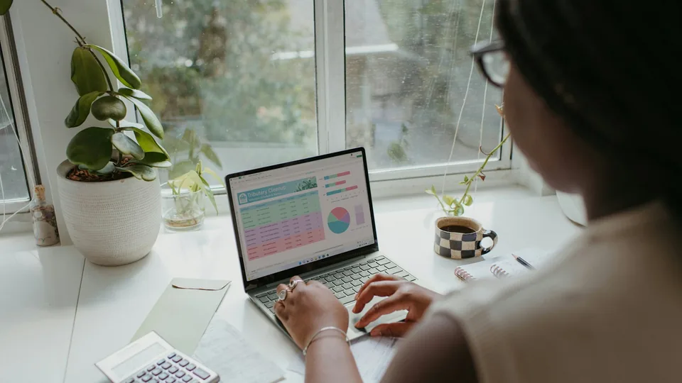 Étudiante consultant un tableau de dépenses sur son ordinateur, une calculatrice posée à côté