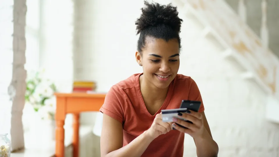 Jeune femme tenant une carte bancaire et son téléphone pour valider une opération