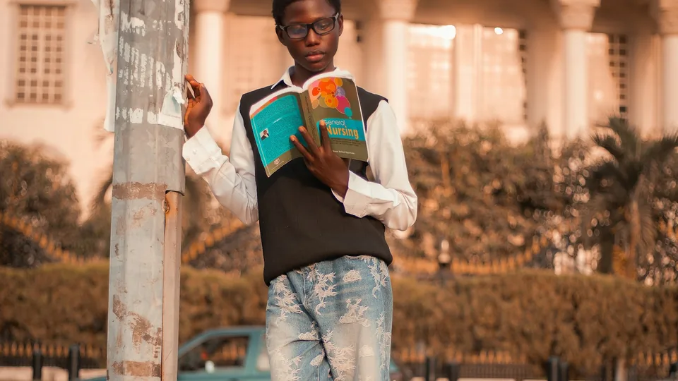 Jeune homme lisant un livre en extérieur pour progresser en langue