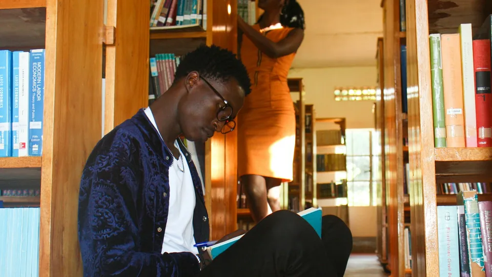 Étudiant consultant un ouvrage entre les rayonnages d'une bibliothèque universitaire