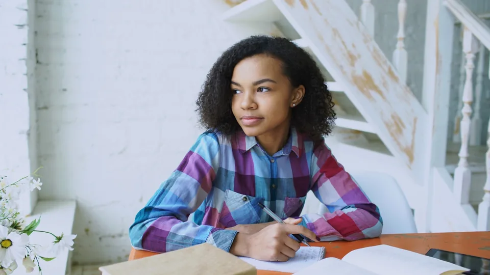 Jeune femme réfléchissant en notant ses questions avant de constituer son dossier